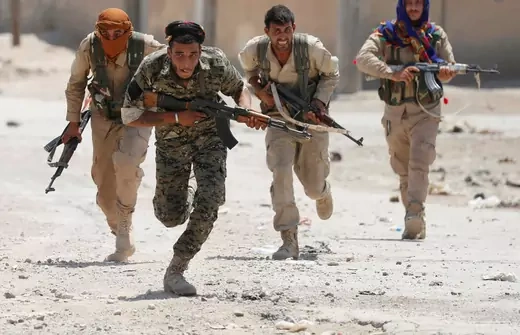 Kurdish fighters from the People's Protection Units (YPG) run across a street in Raqqa, Syria, July 3, 2017.