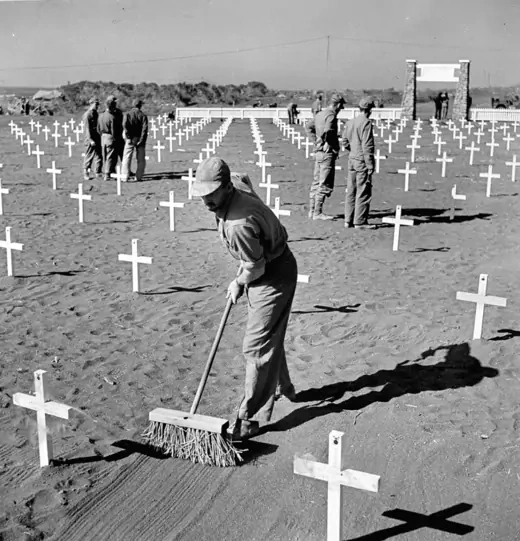 A U.S. Marine smooths the sand between crosses at a 5th division cemetery after the blood battle for Iwo Jima. 