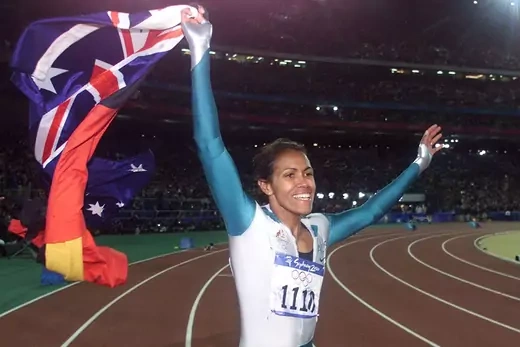 Cathy Freeman smiles and waves both the Aboriginal and the Australian flags on the track.