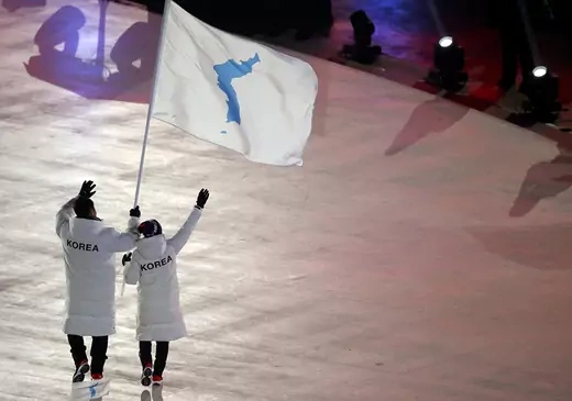 Two people wave a flag showing the Korean Peninsula. 