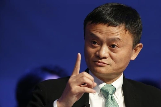 Jack Ma raises his finger and looks away from the camera in front of a blue background.