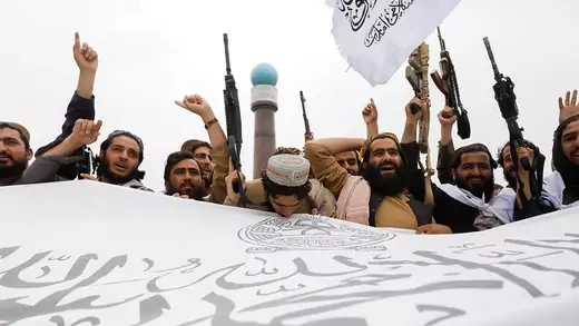 Taliban fighters cheer and hold a flag for the Islamic Emirate of Afghanistan.