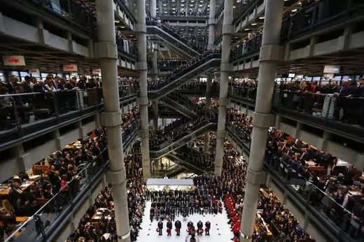 A crowd of people stand on five different floors overlooking an Armistice Day service