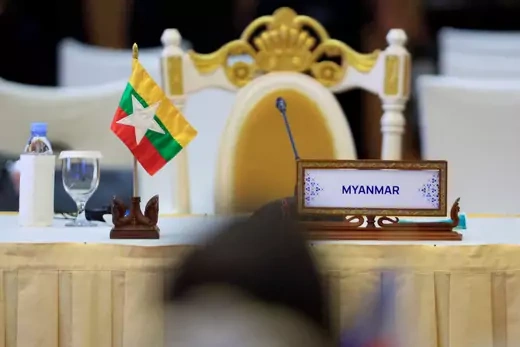 Photo of an unoccupied seat and table holding Myanmar's placard and national flag.