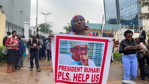 A woman holds a poster of President Muhammadu Buhari that reads "President Buhari Pls Help Us" alongside others in a protest.
