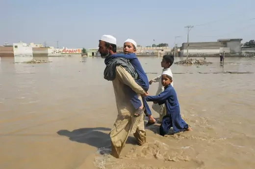 A man walks with children amid flood water along a road, following rains and floods during the monsoon season in Nowshera, Pakistan August 30, 2022. REUTERS/Fayaz Aziz