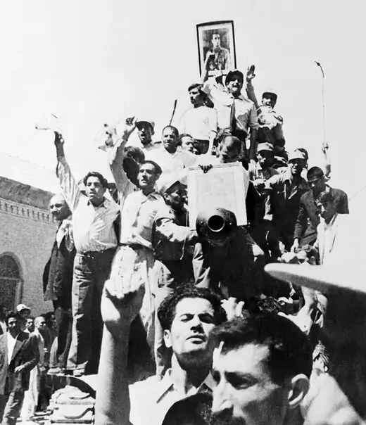 Iranian civilians standing on a tank in Tehran after the 1953 coup. One holds a portrait of the shah.