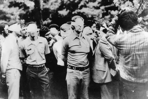 A group of American hostages in Iran stand blindfolded and handcuffed amid their captors.