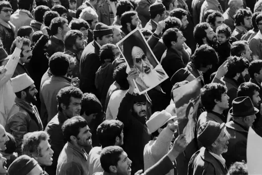 Two men amid a crowd hold up large photos of Grand Ayatollah Ruhollah Khomeini