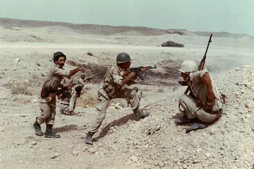 Three soldiers stand in the desert with guns pointed.