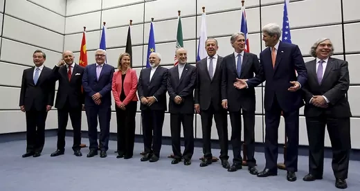 A group of diplomats representing JCPOA signatory countries stand in front of a row of flags 