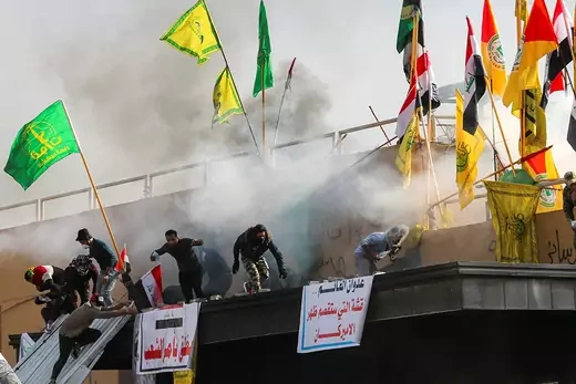 Protesters run away from tear gas at the U.S. embassy in Baghdad, where multiple flags representing Iraqi militias are planted