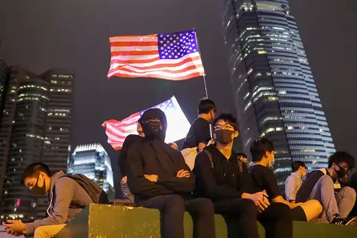 People dressed in black sit by a U.S. flag in Hong Kong. 