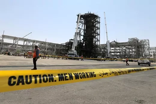Yellow caution tape stretches in front of a Saudi Aramco oil facility