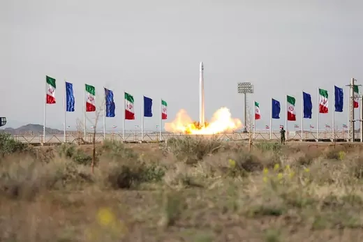 A military satellite launches from behind a row of Iranian flags