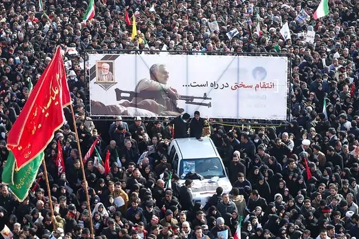 A crowd surrounds a car carrying a banner depicting Iranian Quds Force commander Qasem Soleimani