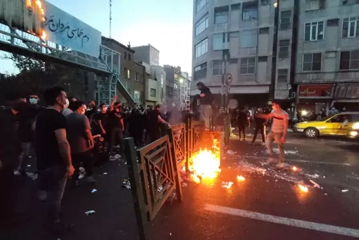 Protestors in Iran stand behind a burning gate.