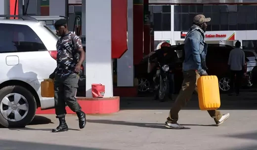 A man and police officers walk in opposite directions holding petrol while at a gas station in Nigeria.
