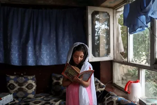 An Afghan girl reads a book inside her home in Kabul, Afghanistan