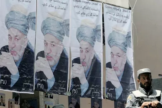 An Afghan policeman sit in front of campaign posters of Hamid Karzai. 
