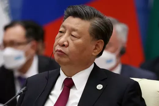 Xi Jinping sits looking to the right of the camera with a earpiece in and a microphone in front of him.