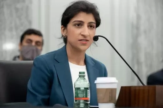 Lina Khan sits at a desk with a small microphone in front of her.