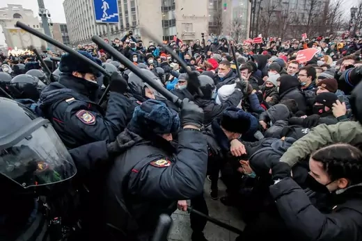 Russian police raise nightsticks to hit a group of protestors.