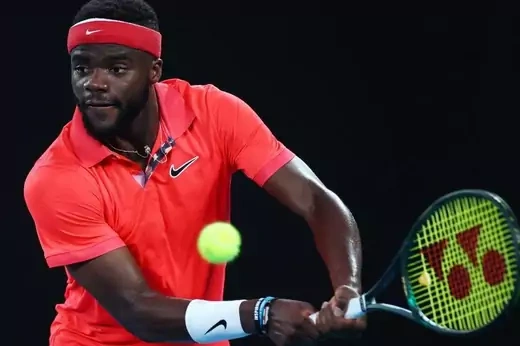 Frances Tiafoe, in a red shirt and red headband, in mid-swing with a tennis ball in the frame.