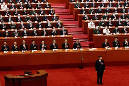 Xi Jinping stands on a red carpet ahead of lawmakers seated behind him in ascending rows.