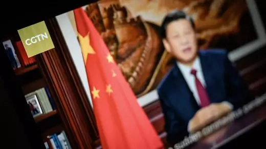 A screen displays a CGTN broadcast of Xi Jinping giving a speech. 