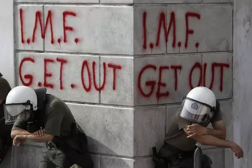 Greek riot policemen rest in front of graffiti written on the wall of a bank in Athens during violent demonstrations.