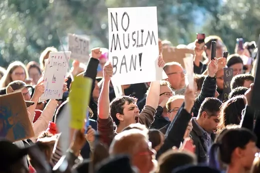 A man holding up a sign reading "No Muslim Ban" stands among protesters.