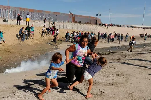 A migrant woman from Honduras, part of a caravan of thousands from Central America, runs from tear gas with her five-year-old daughters at the U.S.-Mexico border.