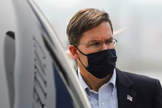 A close-up shot of Defense Secretary Mark T. Esper wearing a black face mask, glasses, and a suit.