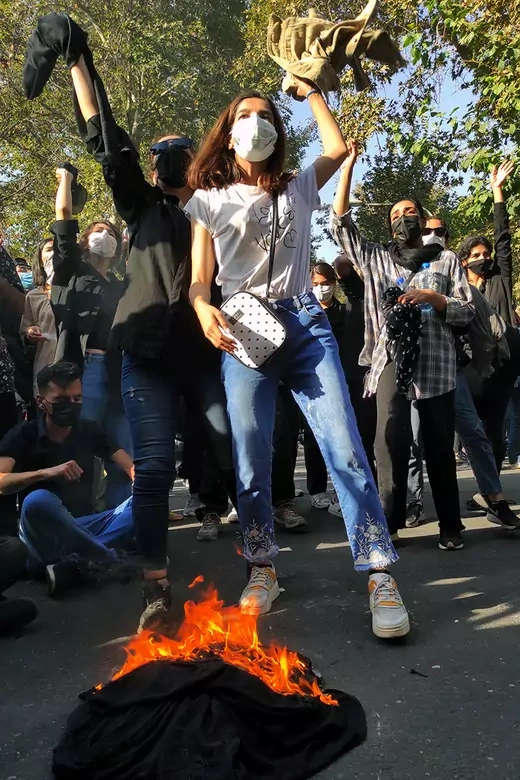 Iranian protesters set their headscarves on fire while marching down a street in Tehran.