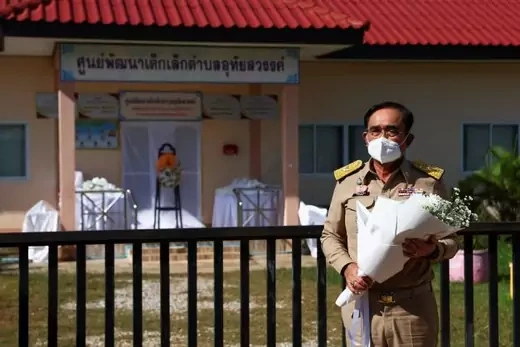 Prime Minister of Thailand Prayuth Chan-ocha stands outside of the daycare where a mass shooting took place, holding a bouquet of flowers.