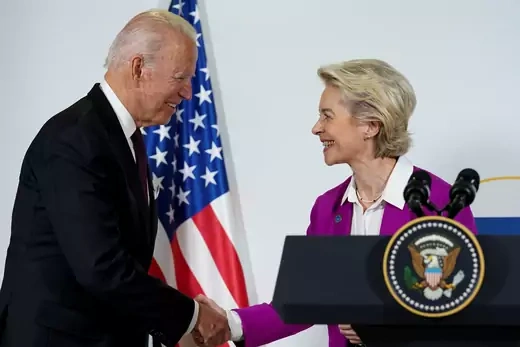 Joe Biden and Ursula von der Leyen shake hands in front of an American flag.