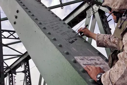 A US Marine of the 1st Division writes the words "Dark Horse" on a beam of the bridge western Fallujah, Iraq, where the bodies of two American contractors killed by militants were strung.