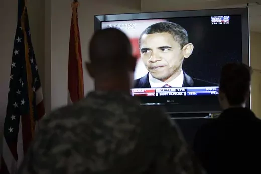 A U.S. soldier and an embassy official watch U.S. President-elect Barack Obama on television.