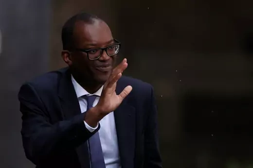 Kwasi Kwarteng raises his hand to wave at supporters and reporters.