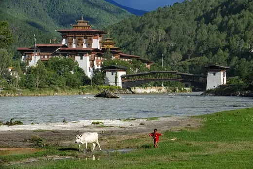 A monastery sits in between tree-covered mountains.   