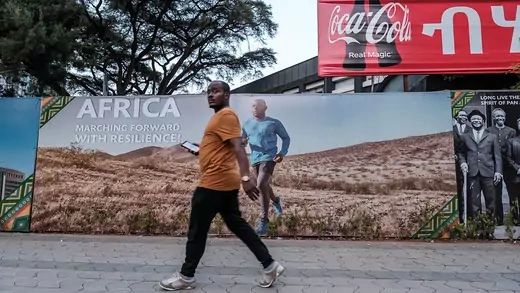 A man walks by a large billboard sign that reads "Africa: Marching Forward With Resilience!"
