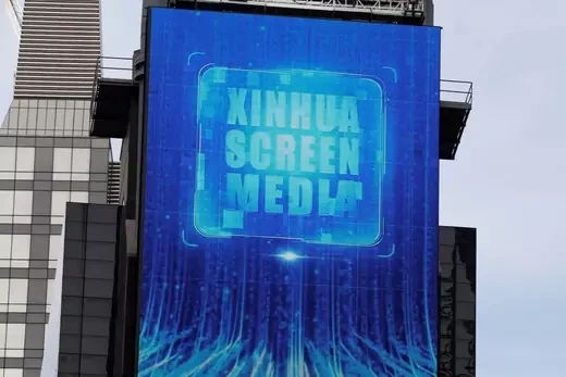 A large blue screen on a building in Times Square, New York City, advertises  "Xinhua Screen Media.""
