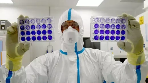 A scientist holds up two trays of cells.