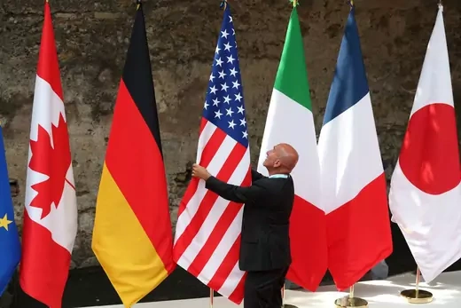 A bald man adjusts a Canadian, German, U.S., Italian, French, and Japanese flag.