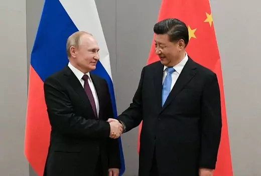 Vladimir Putin shakes hands with Xi Jinping in front of a Russian flag and a Chinese flag.