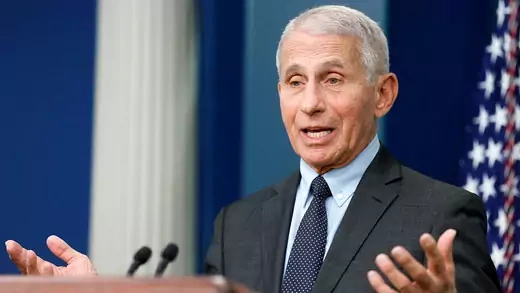 Fauci speaking at a podium with the US flag behind him
