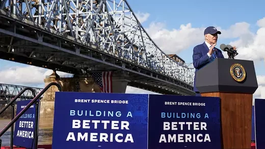 Biden speaking at podium in front of bridge next to "building a better america" signs