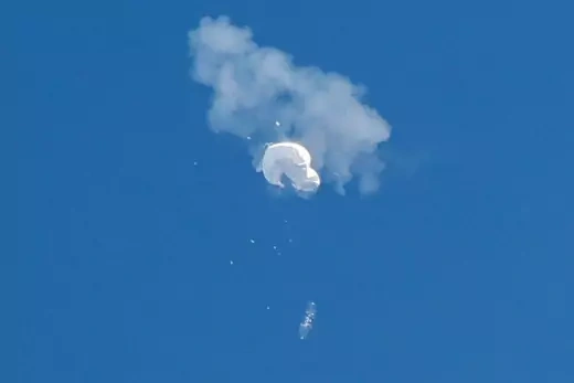 A cloud of white smoke around a while balloon drifting in the sky.