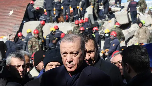 Turkish President Recep Tayyip Erdogan seen as relief workers behind him search rubble from an earthquake